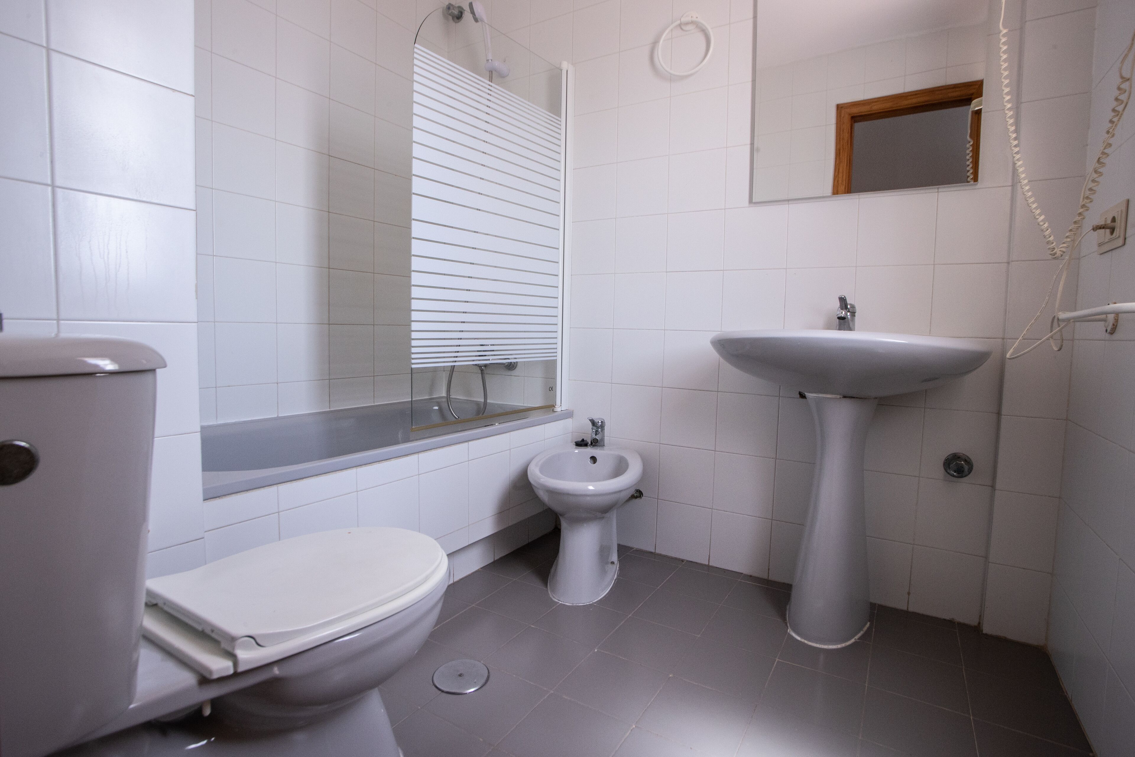 A bathroom with a toilet, bidet, sink, and a shower enclosure.