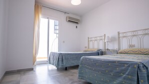 Ein Zimmer mit zwei Betten, einem Fenster mit Vorhängen, einer Klimaanlage und einem Nachttisch mit Lampe.
