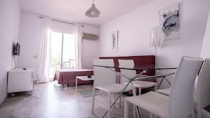 Ein modernes Hotelzimmer mit einem Glastisch, weißen Stühlen, einem roten Sofa und einer Deckenleuchte.