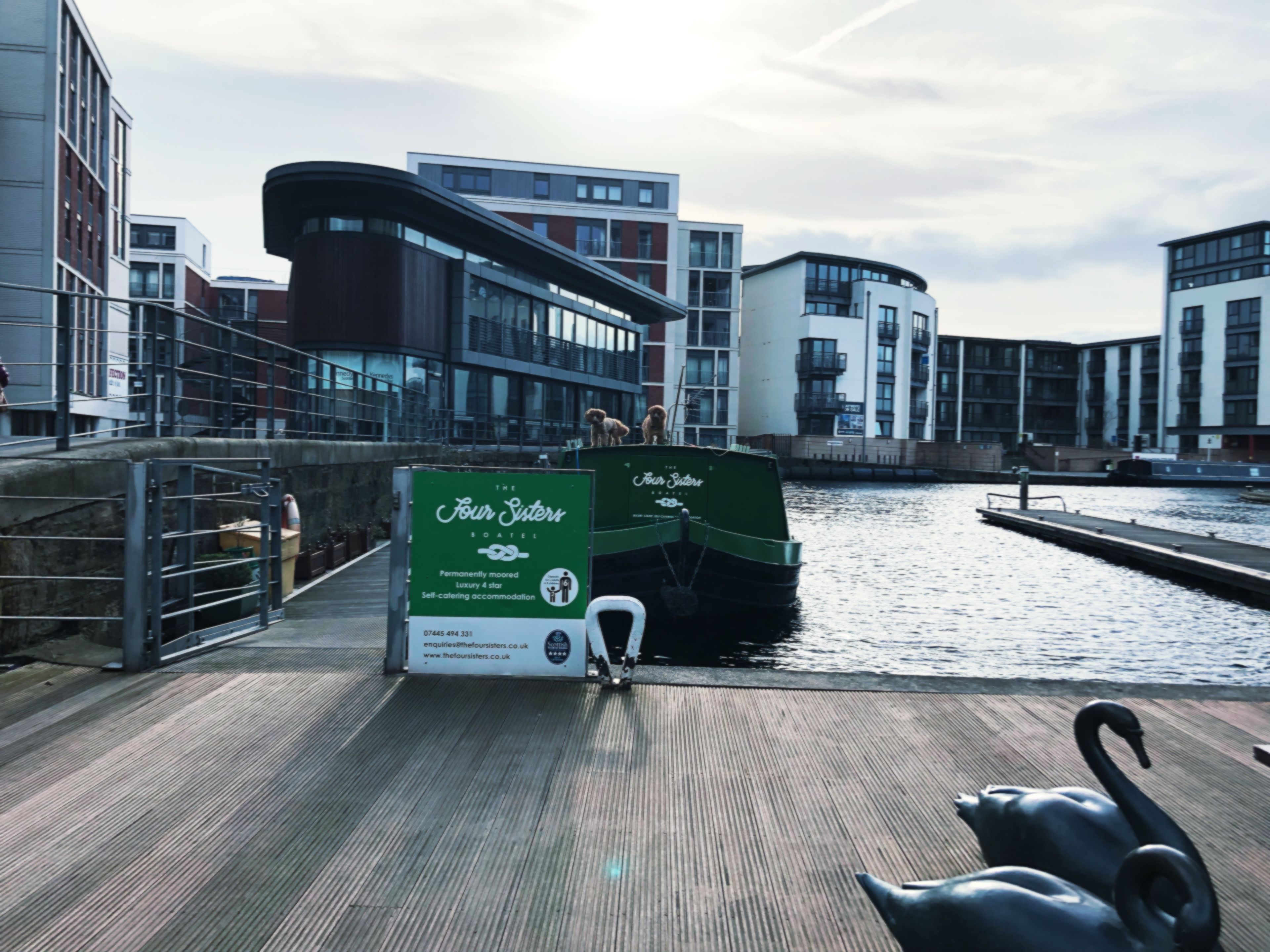 A green boat docked at a waterfront with modern buildings in the background.