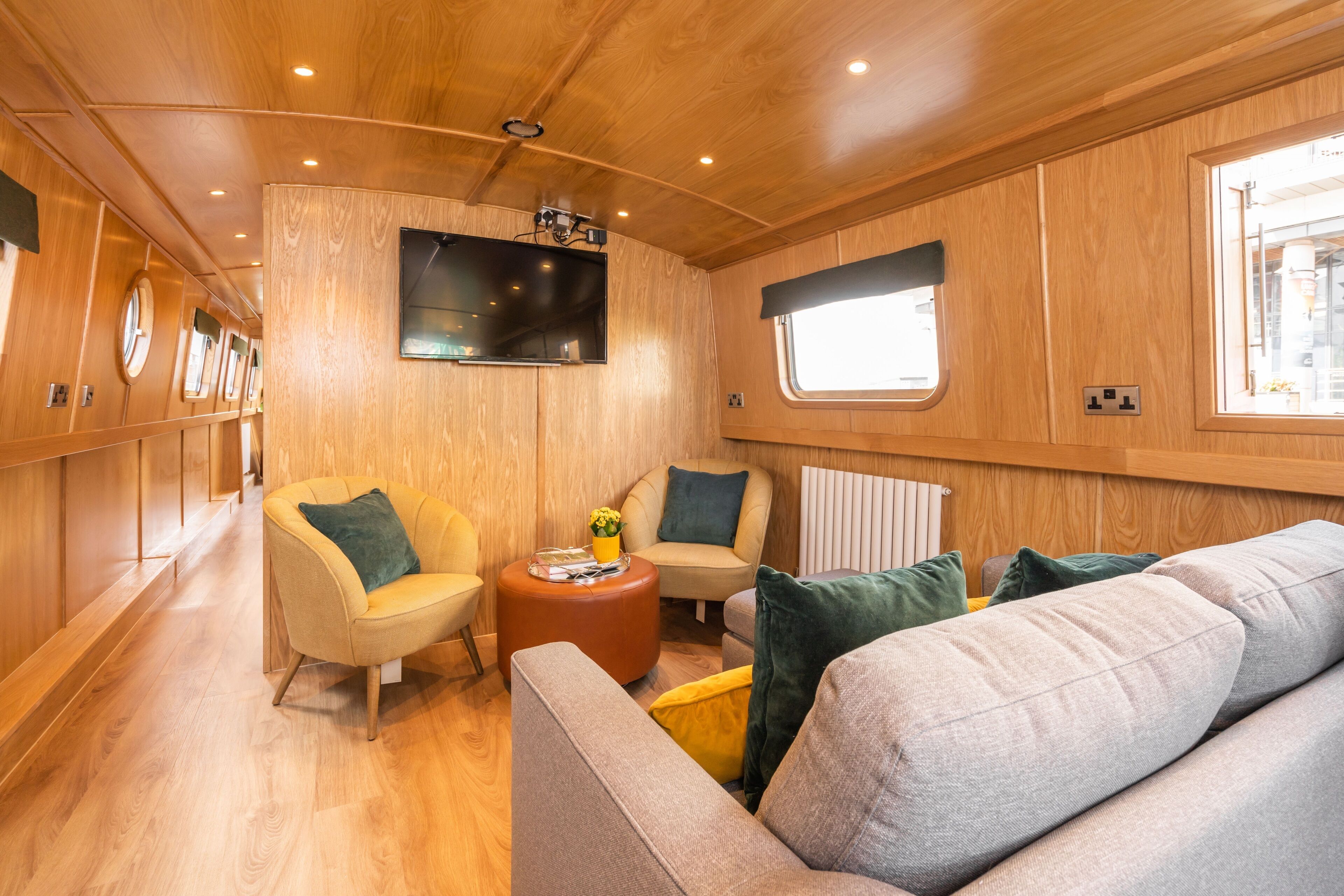 A cozy interior with wooden paneling, a sofa, two armchairs, a coffee table, and a television mounted on the wall.