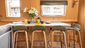 A compact kitchenette with wooden cabinetry, a small dining table, and three bar stools. - The Four Sisters Boatel (Edinburgh)