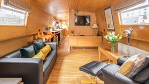 A cozy interior with a sofa, a small table, and a TV mounted on the wall. - The Four Sisters Boatel (Edinburgh)