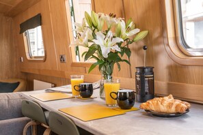 A breakfast setup with a croissant, coffee pot, and juice glasses on a table with a vase of flowers. - The Four Sisters Boatel (Edinburgh)