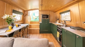 A compact kitchen with wooden cabinets, a microwave, and a sink. - The Four Sisters Boatel (Edinburgh)