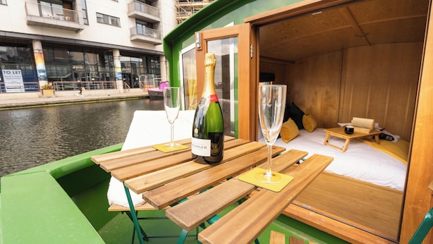 A green boat with a wooden deck, a bottle of wine, and two glasses on the table. - The Four Sisters Boatel (Edinburgh)