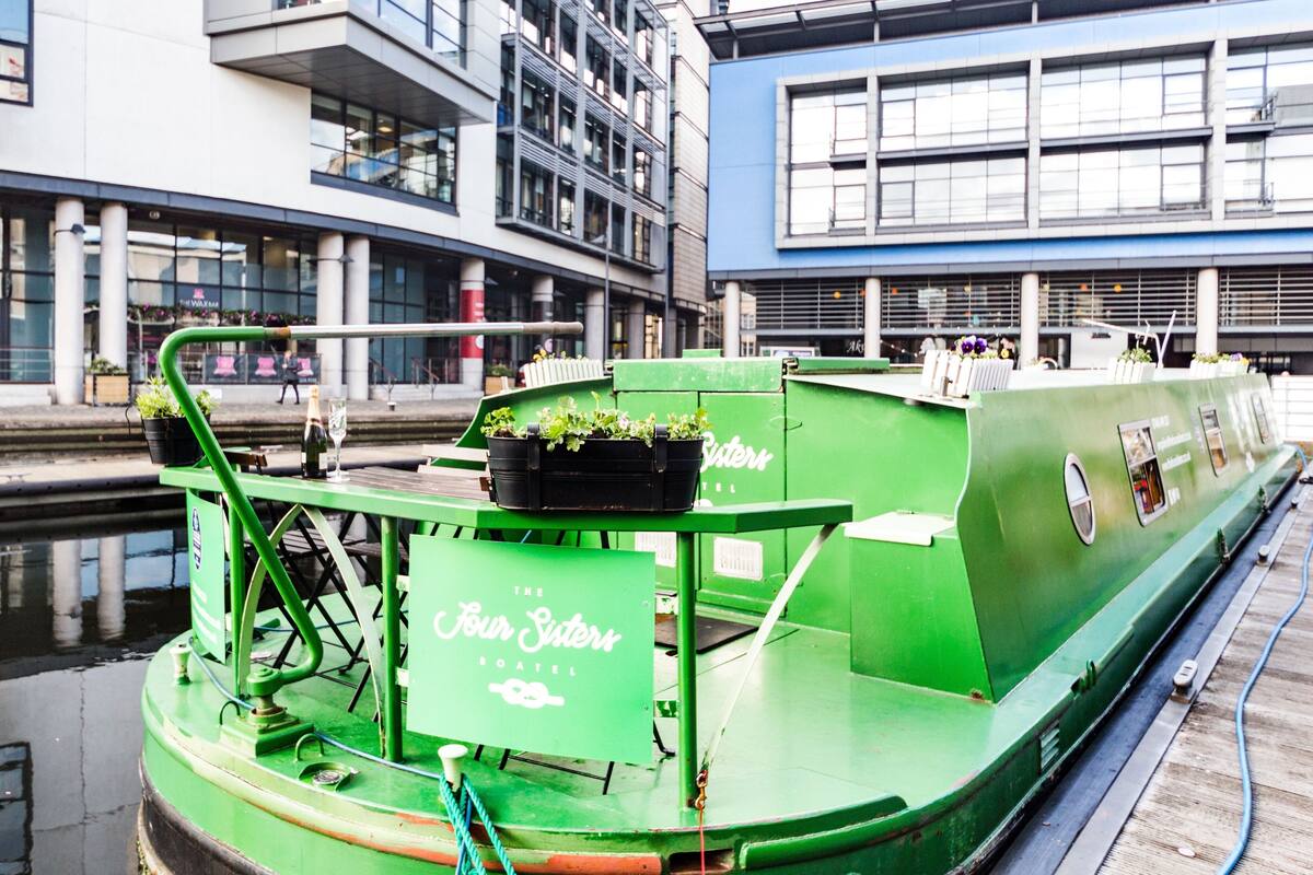 A green boat with a sign reading "The Four Sisters Boatel" docked at a canal.