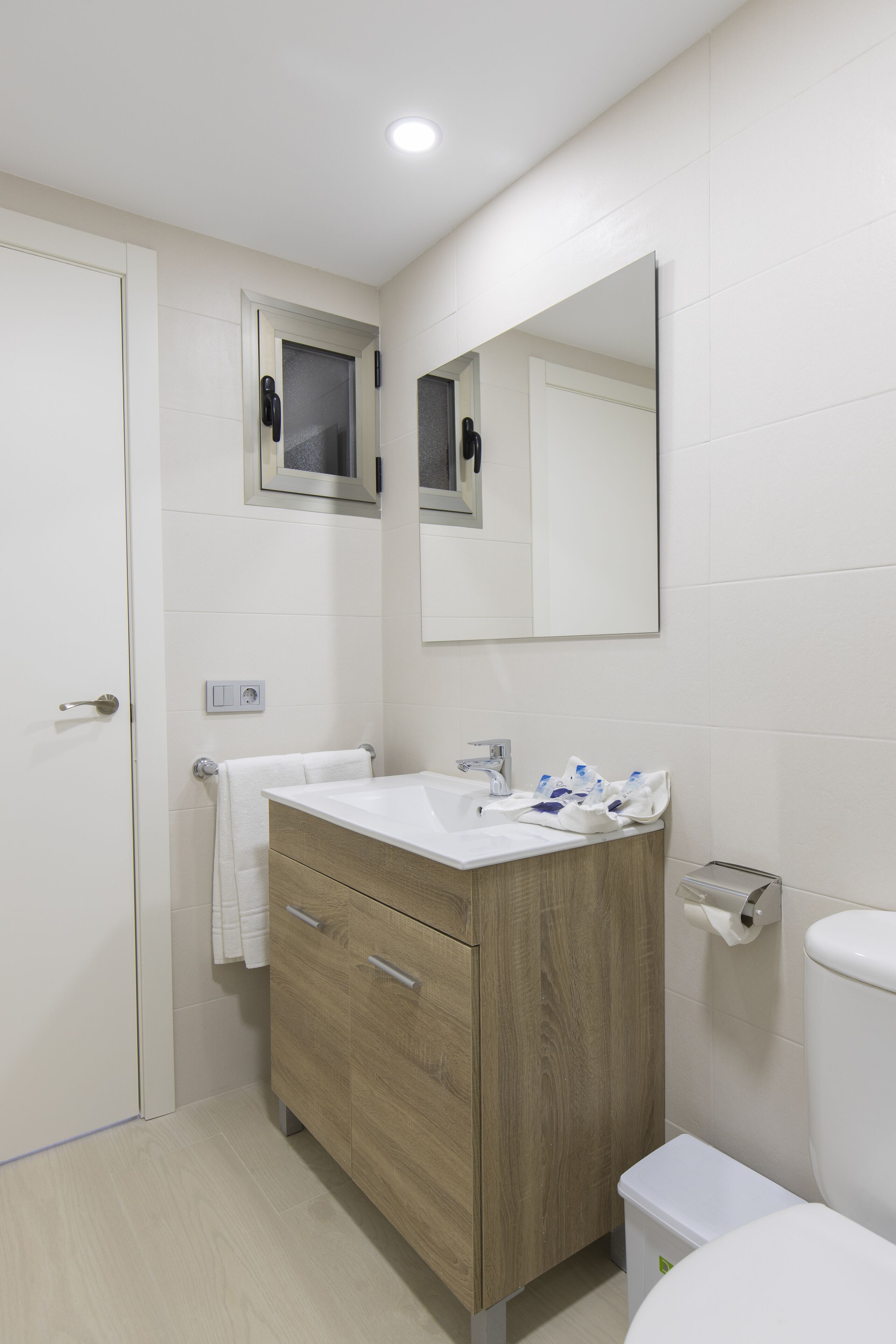 Ein Badezimmer mit einem Holzkosmetikschrank, einem Spiegel, einer Toilette und einem Waschbecken.
