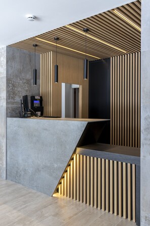 Een moderne receptiebalie met een betonvloer, houten lamellen en hanglampen.