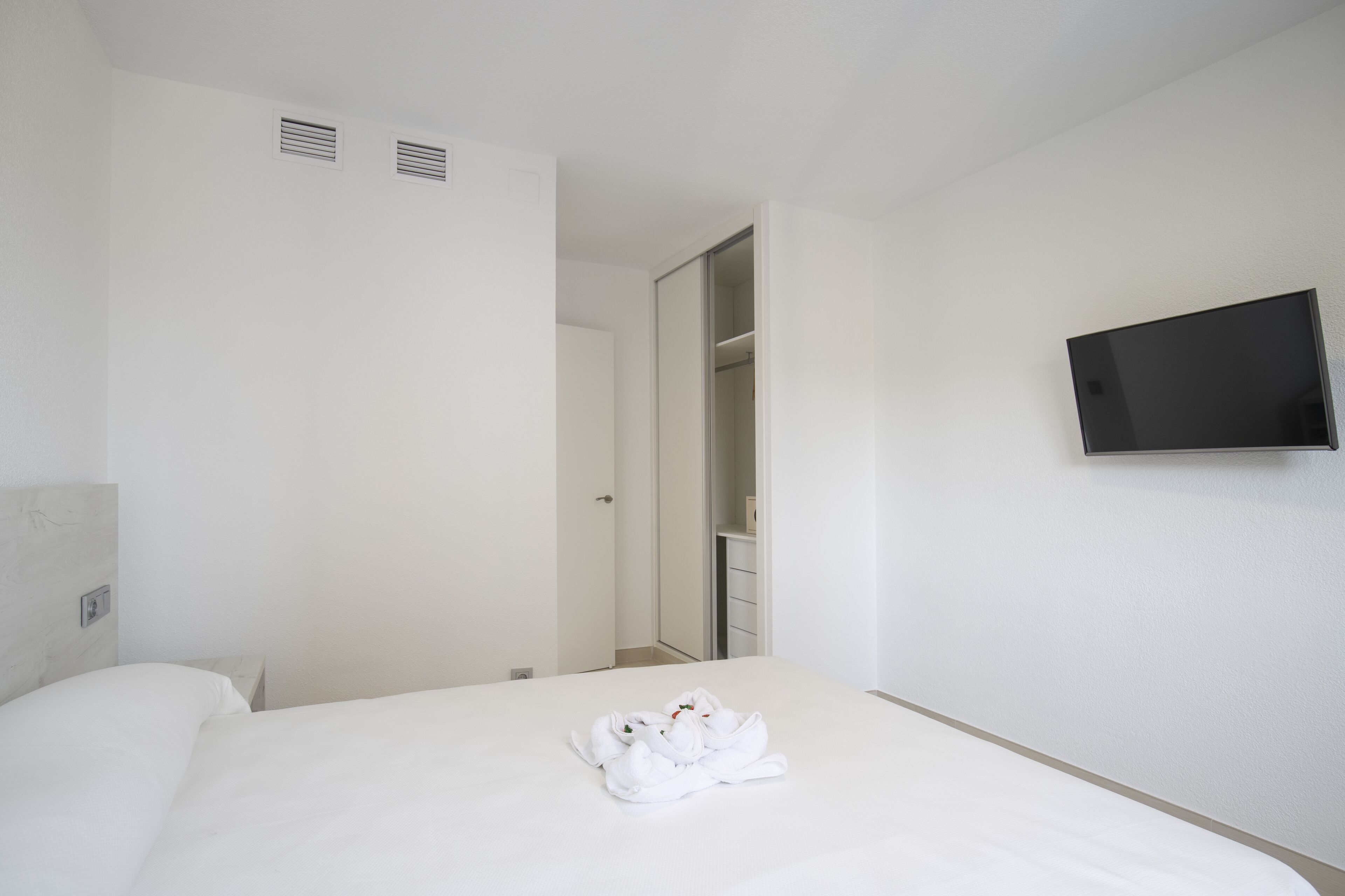 A hotel room with a bed, a flat-screen TV mounted on the wall, and a bathroom visible through an open door.