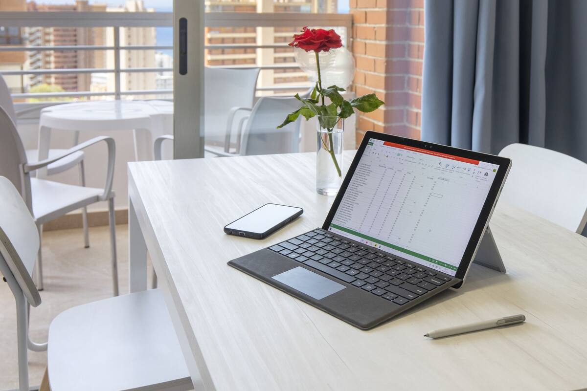 Un balcón con una laptop, una rosa y un teléfono inteligente sobre una mesa.