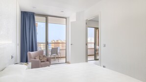 Ett hotellrum med en säng, en stol, ett bord och utsikt över staden genom en balkongdörr.