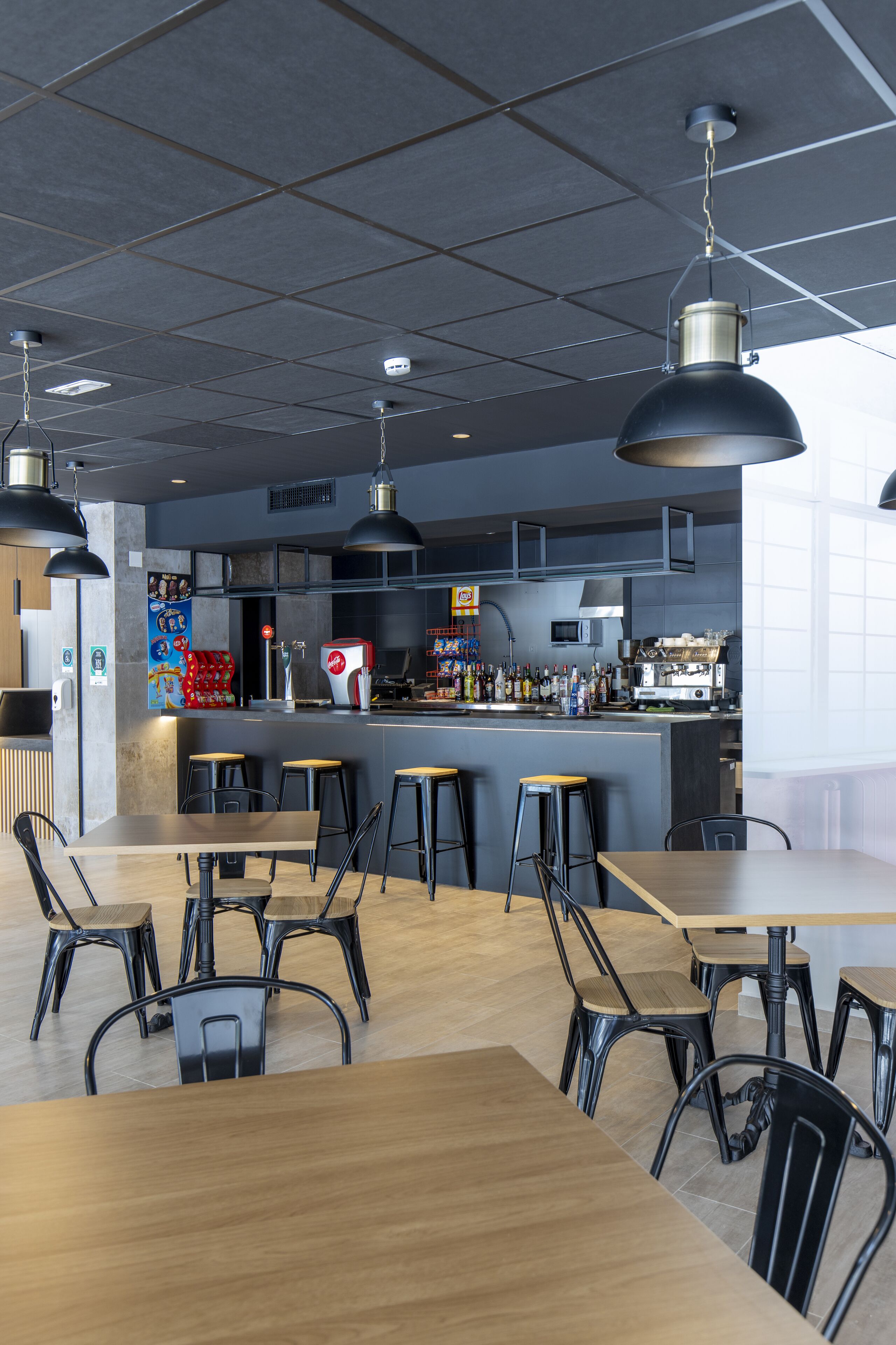 A modern restaurant with a bar area, wooden tables, and black metal chairs.