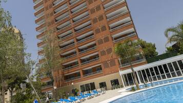 Un hotel moderno con piscina, sillas de descanso azules y cielo despejado.