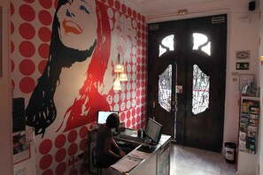 A reception area with a large wall mural, a reception desk, and a door marked "SALIDA". - Red Nest Hostel (Valencia)