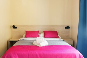 A neatly made bed with pink and white bedding, two red pillows, and a folded towel on the bed. - Red Nest Hostel (Valencia)