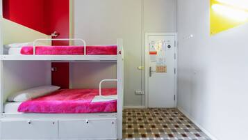 Une chambre de dortoir avec des lits superposés, une porte sur laquelle est accroché un tableau d’affichage et un sol à motifs.