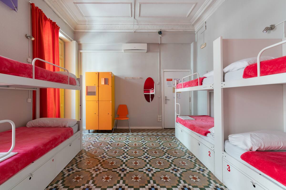 Un dormitorio con literas, suelo estampado, un escritorio pequeño naranja y un espejo con marco rojo.