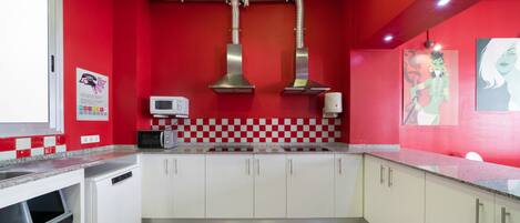 Una cocina con paredes rojas, armarios blancos, un microondas y un cubo de basura.