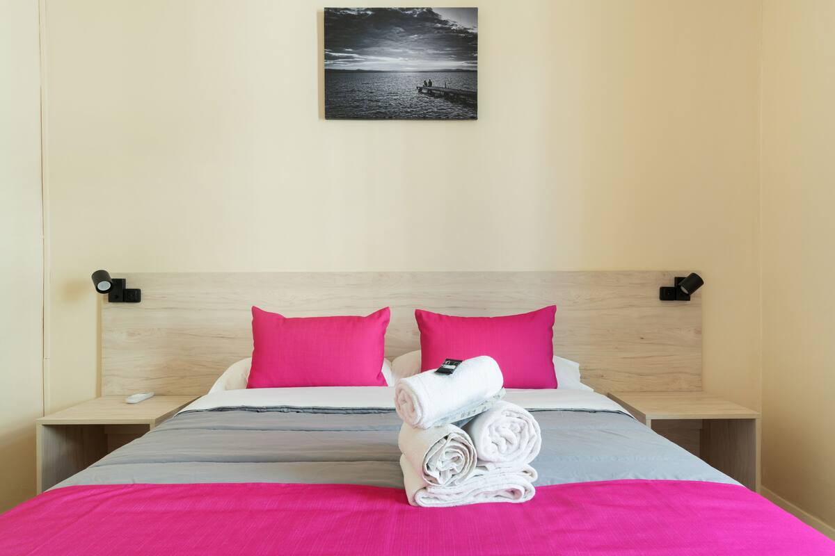 Habitación de hotel con cama, dos almohadas, mesita de noche con teléfono y un cuadro en la pared.
