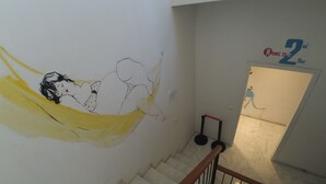 A staircase with a hand-painted mural, a sign indicating rooms 23-42 on the 2nd floor, and a blue decorative element on the wall. - The Spot Central Hostel (Seville)