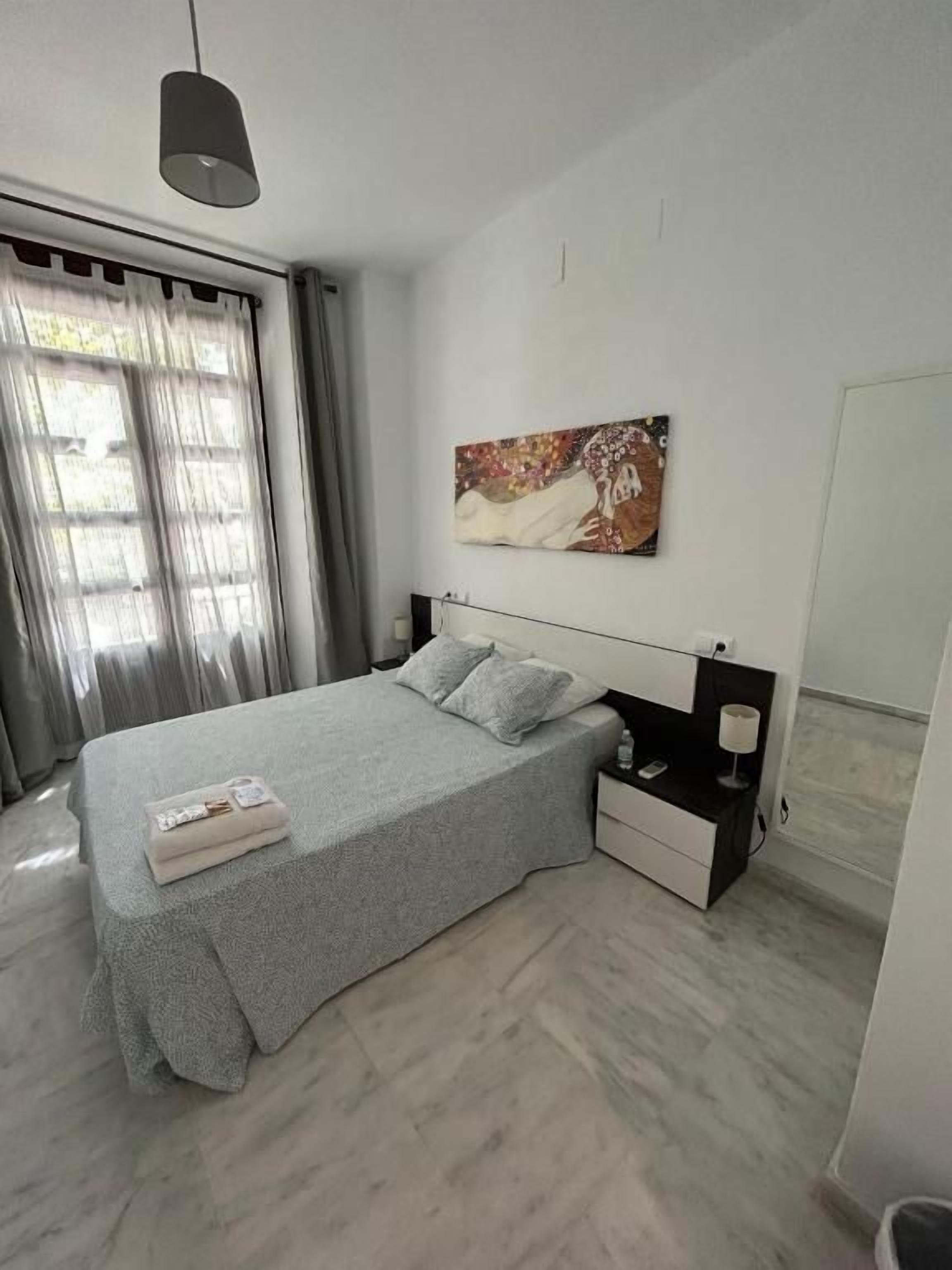 Une chambre à coucher avec un lit, une table de chevet, une lampe et une œuvre d’art accrochée au mur.