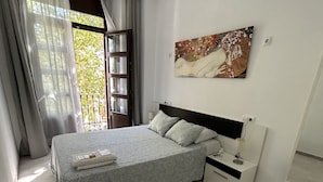 A bedroom with a bed, a nightstand, a painting, and a window with curtains. - The Spot Central Hostel (Seville)