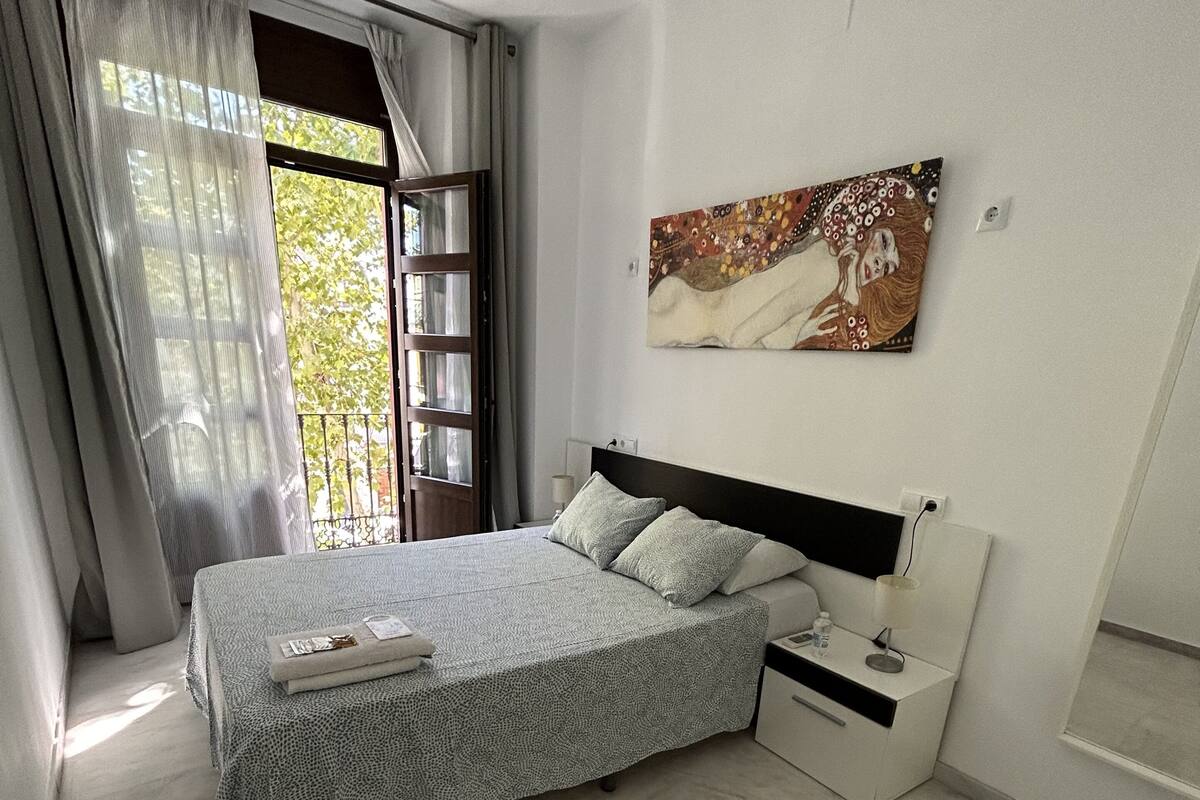 Quarto com cama, mesa de cabeceira, um quadro e janela com cortinas.
