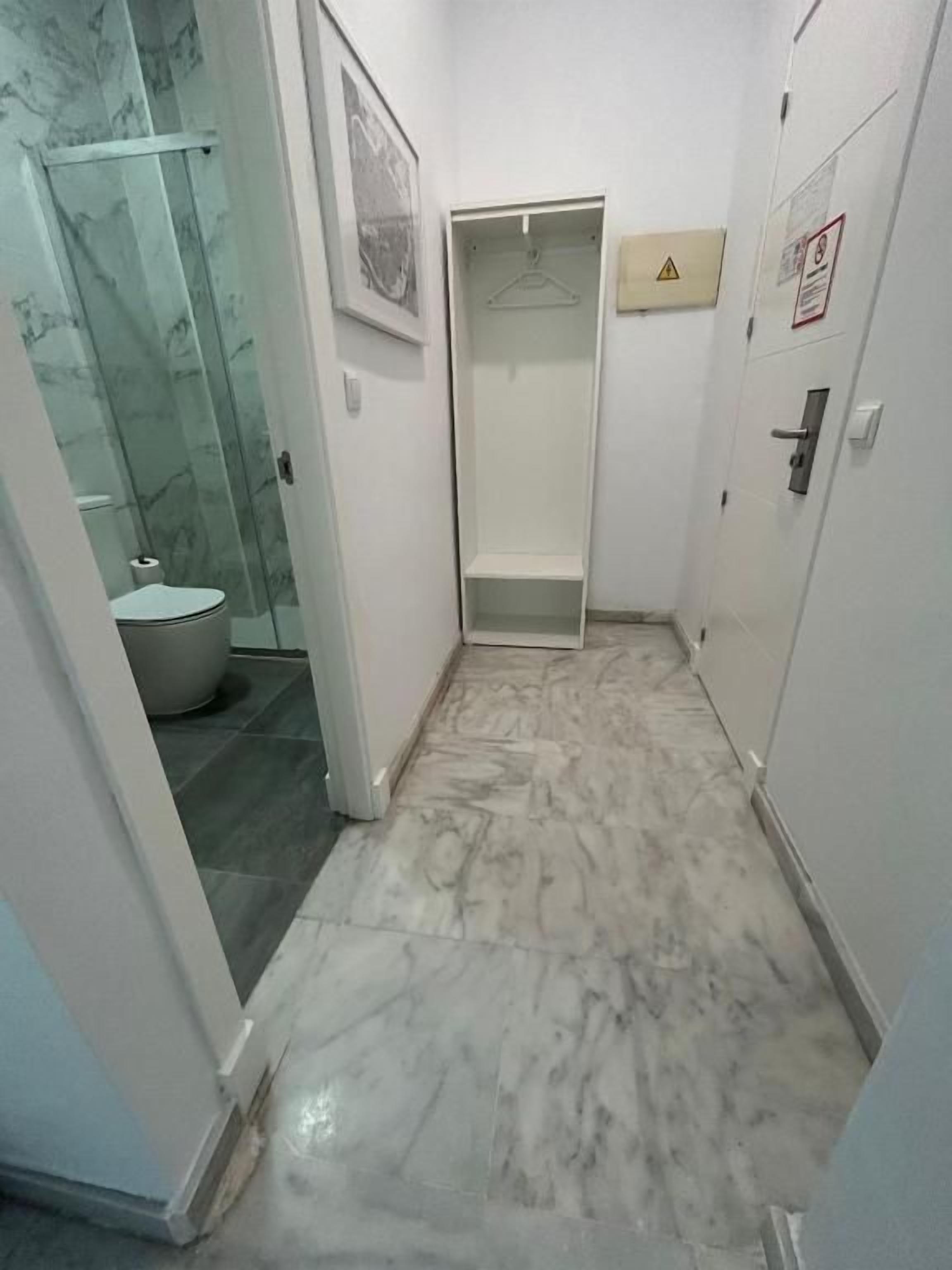 A narrow hallway with a glass shower enclosure, a toilet, and a door with a hanger.