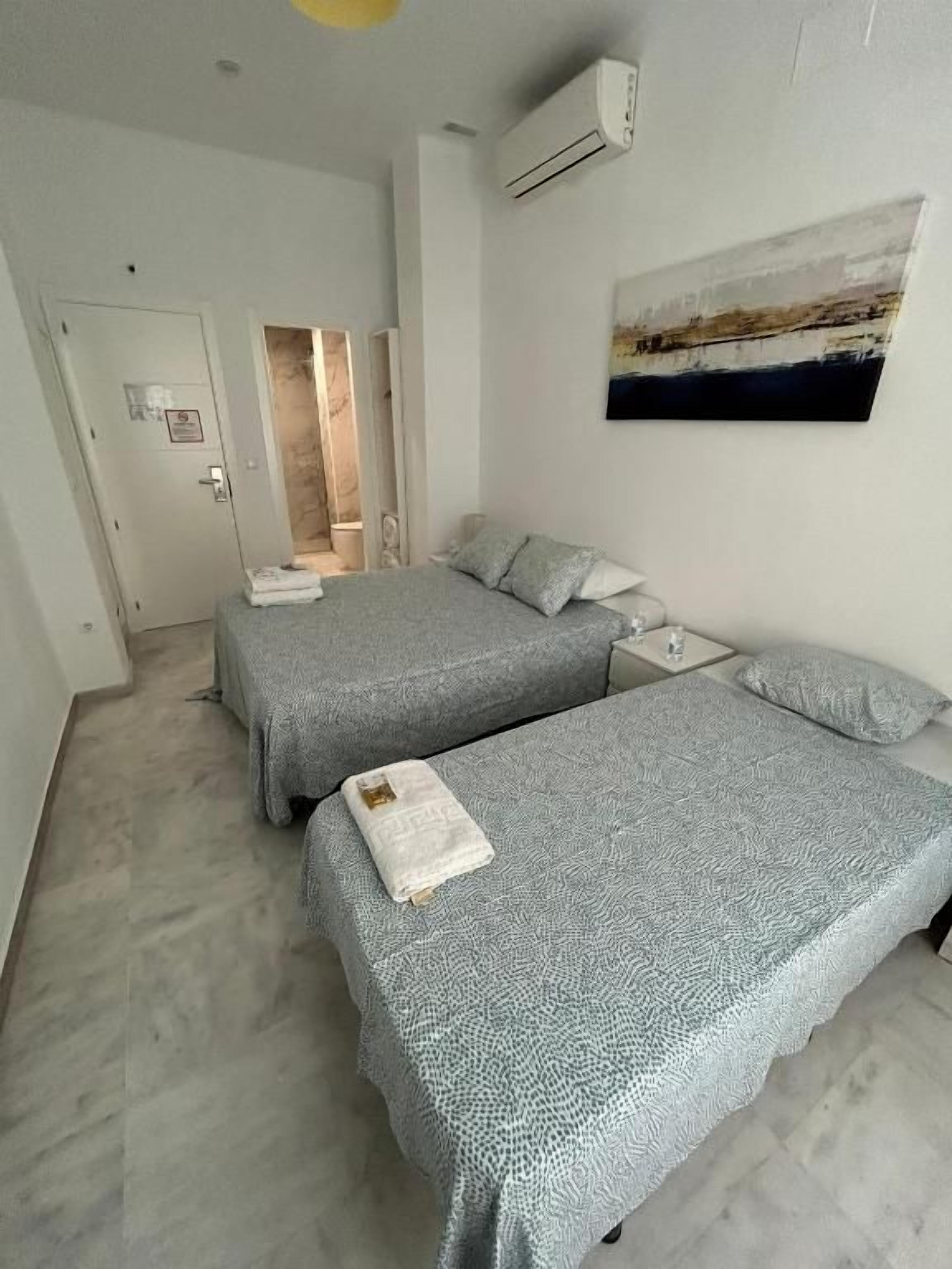 Habitación de hotel con dos camas, un cuadro en la pared y una puerta que da a un baño.