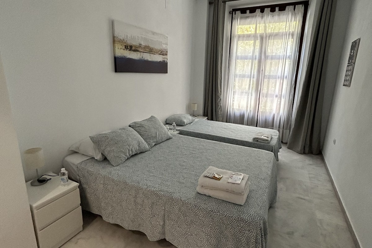 Quarto com cama grande, mesa de cabeceira, abajur e janela com cortinas.