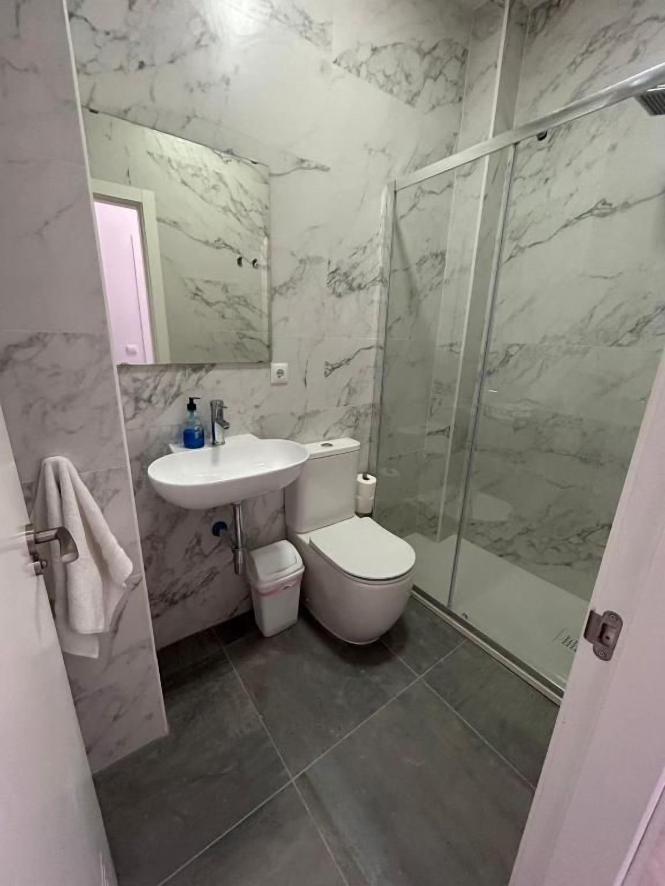 Un baño con pared de mármol, cabina de ducha de vidrio, lavamanos y retrete.