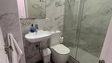Un baño con pared de mármol, cabina de ducha de vidrio, lavamanos y retrete.