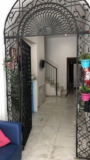 A hallway with a black metal gate, a staircase, and potted plants. - The Spot Central Hostel (Seville)