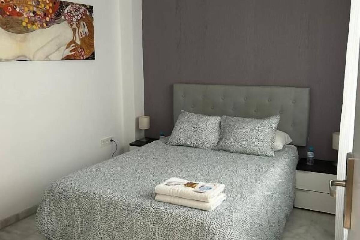 Quarto moderno com colcha cinza estampada, cabeceira estofada cinza e uma mesa de cabeceira com luminária.