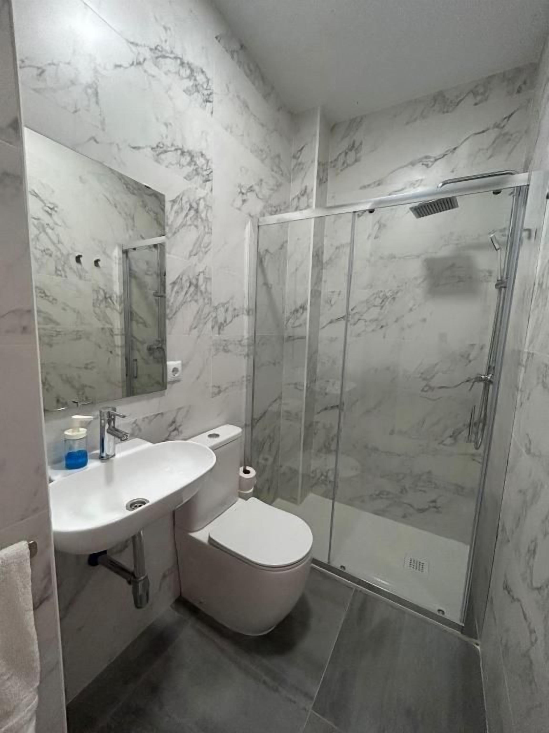 A bathroom with a marble wall, a toilet, a sink, and a glass shower enclosure.