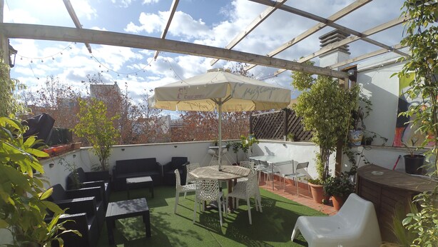 A covered patio area with a table and chairs, a sofa, and potted plants. - The Spot Central Hostel (Seville)