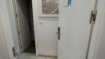 Un couloir étroit avec une porte portant un panneau indiquant qu’il est accessible aux personnes en fauteuil roulant, une fenêtre donnant sur le paysage urbain et un sol carrelé.