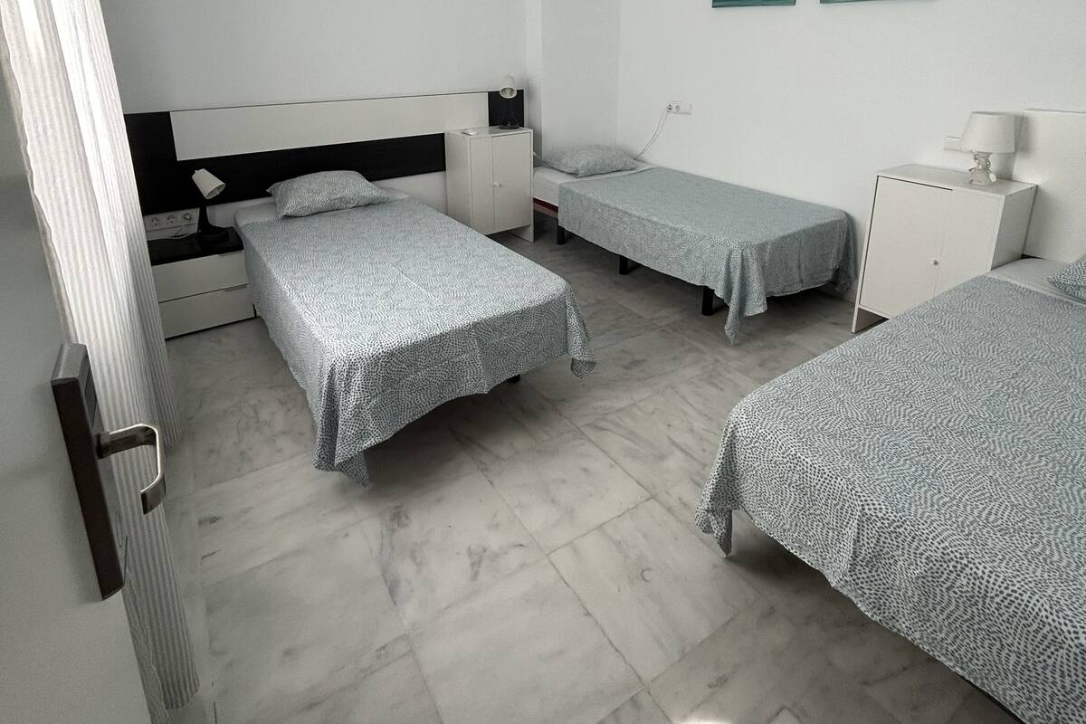 Quarto com três camas de solteiro, um guarda-roupa branco, uma escrivaninha com luminária e duas pinturas na parede.