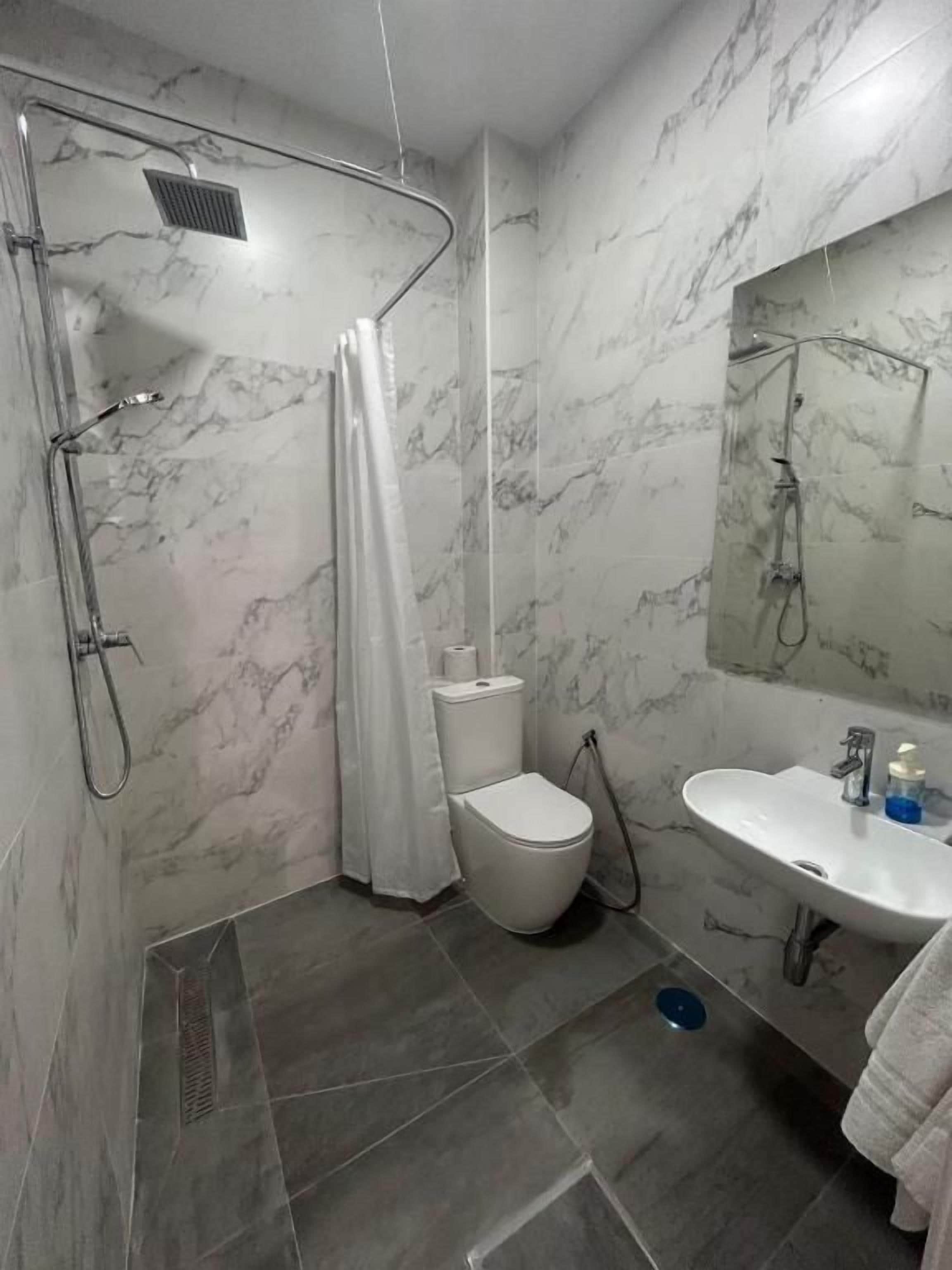 Een badkamer met douche, toilet, wastafel en spiegel.