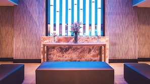 A reception area with a marble counter, two vases with plants, and a bench.