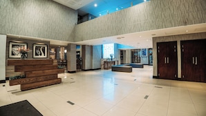 Eine geräumige Lobby mit hoher Decke, einem Empfangstresen und einer Treppe zu einer oberen Ebene.