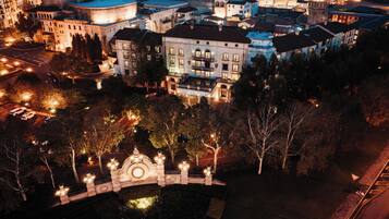 An aerial view of a historic cityscape with a prominent hotel labeled 'Piazza Hotel' featuring classical architecture, a central courtyard with a decorative fountain, and surrounding urban buildings.