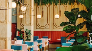 En restaurantindretning med træpaneelvægge, hængende pendellamper og siddepladser i blå og pink farver.