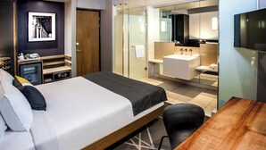 Ein Hotelzimmer mit einem Bett, einem Schreibtisch, einem Spiegel, einem Badezimmer mit Waschbecken und Dusche sowie einem kleinen Schrank.