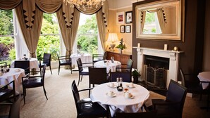 A formal dining room with round tables, black chairs, a chandelier, and a fireplace. - Beaumont House (Cheltenham)