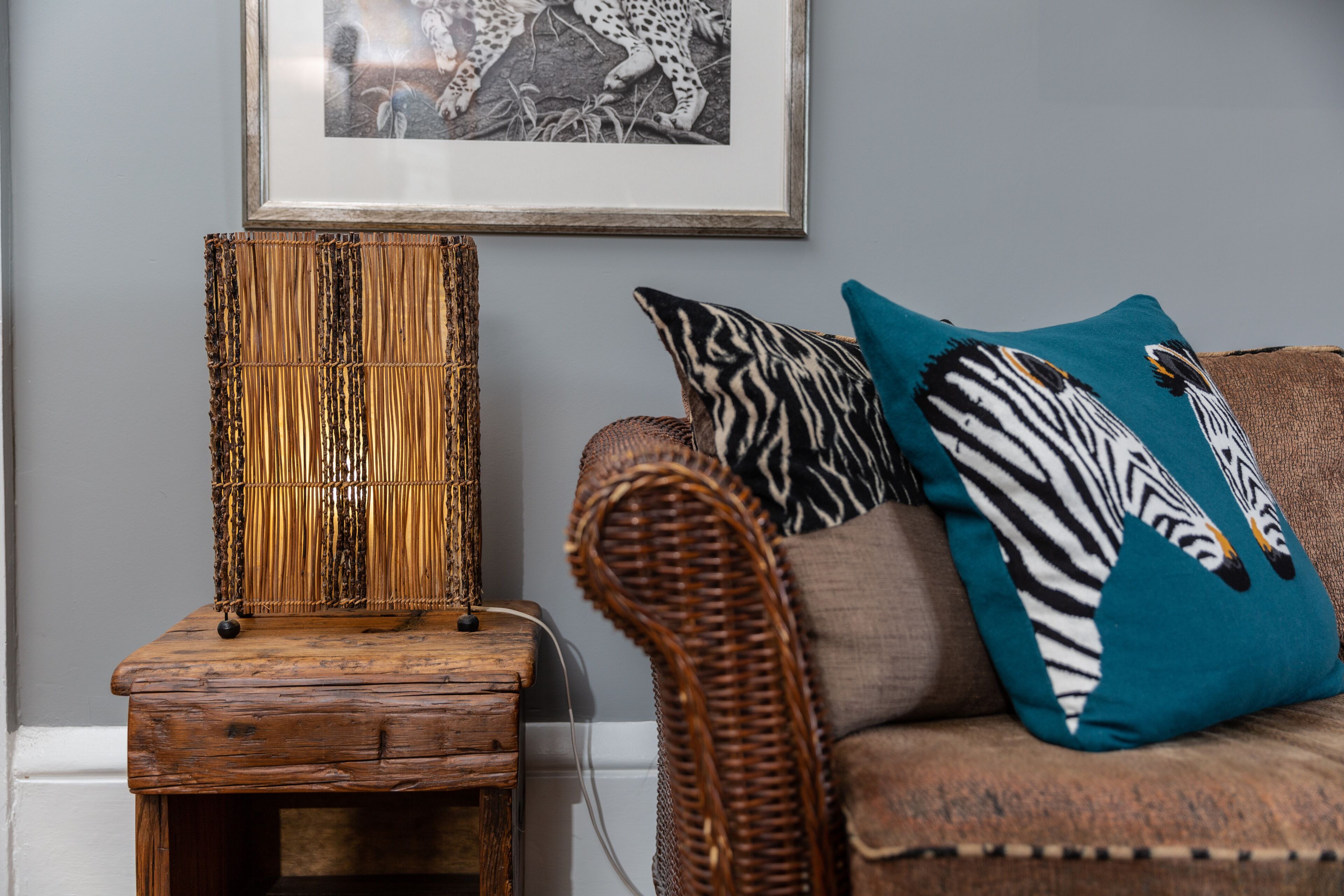 A wicker chair with a cushion and a framed picture on the wall.