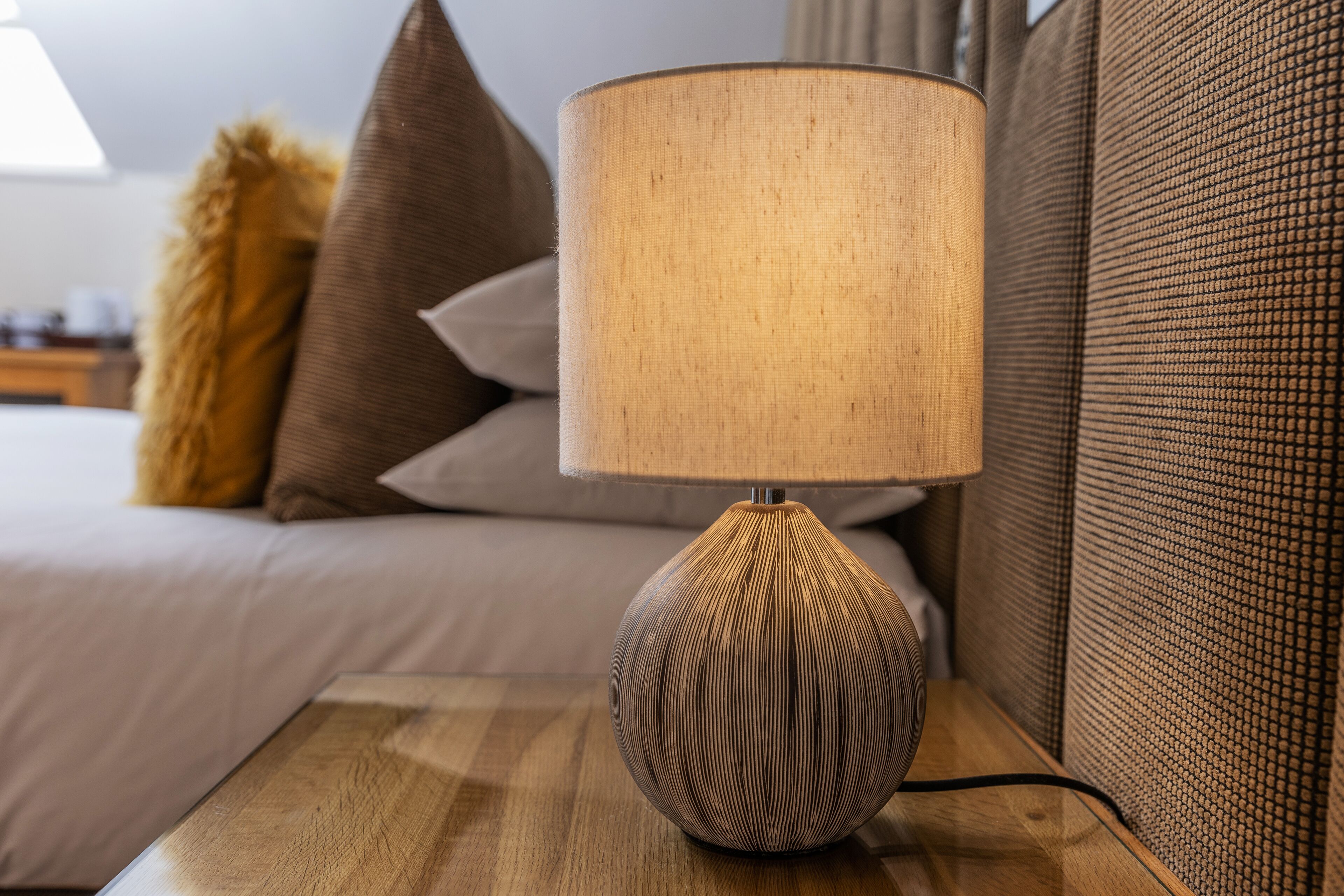 Una lámpara de mesa de madera con una pantalla texturizada sobre una mesita de noche en una habitación de hotel.
