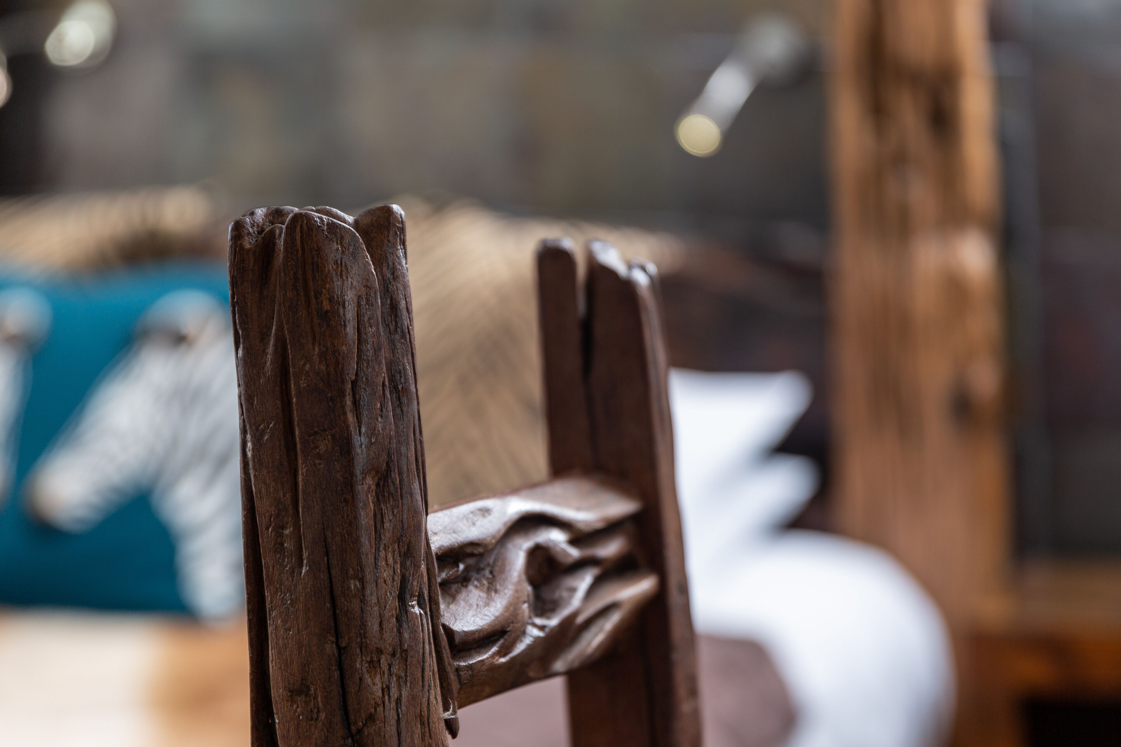 A close-up of a wooden chair with carved details, part of a room with a blurred background.