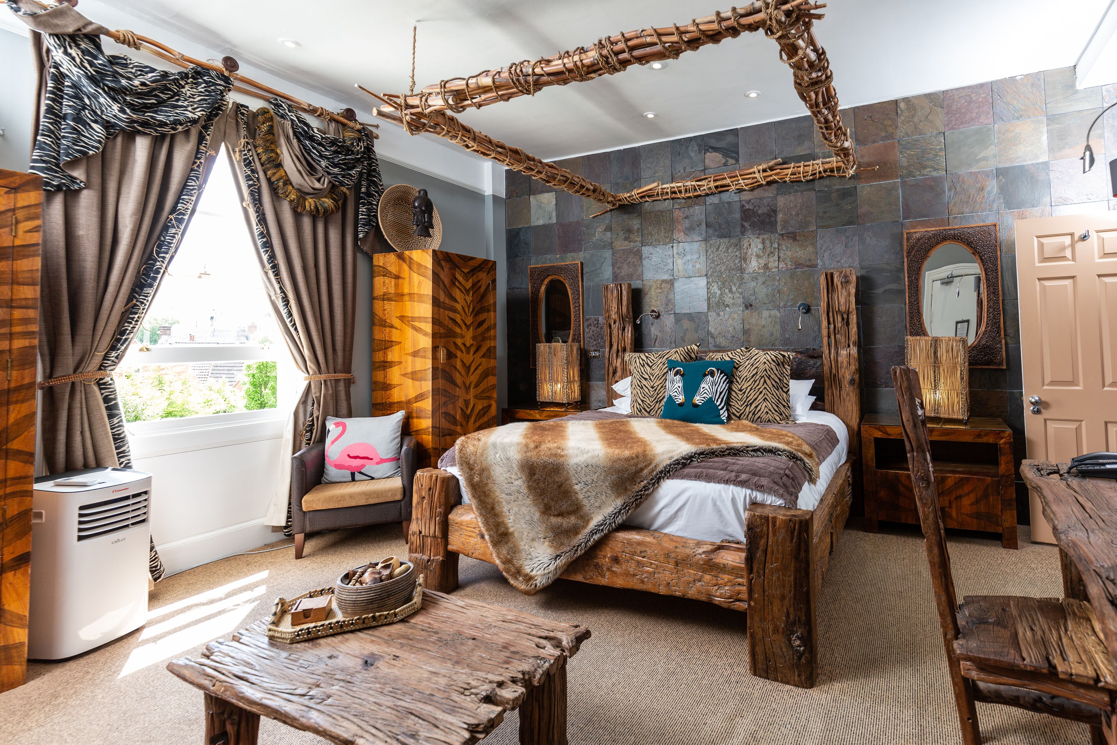 Un dormitorio rústico con una cama grande, muebles de madera, una silla colgante y una pared de piedra.